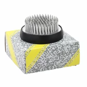 Close-up of a round Kenzan flower frog with sharp brass pins on a solid metal base, for stable and precise floral arranging.